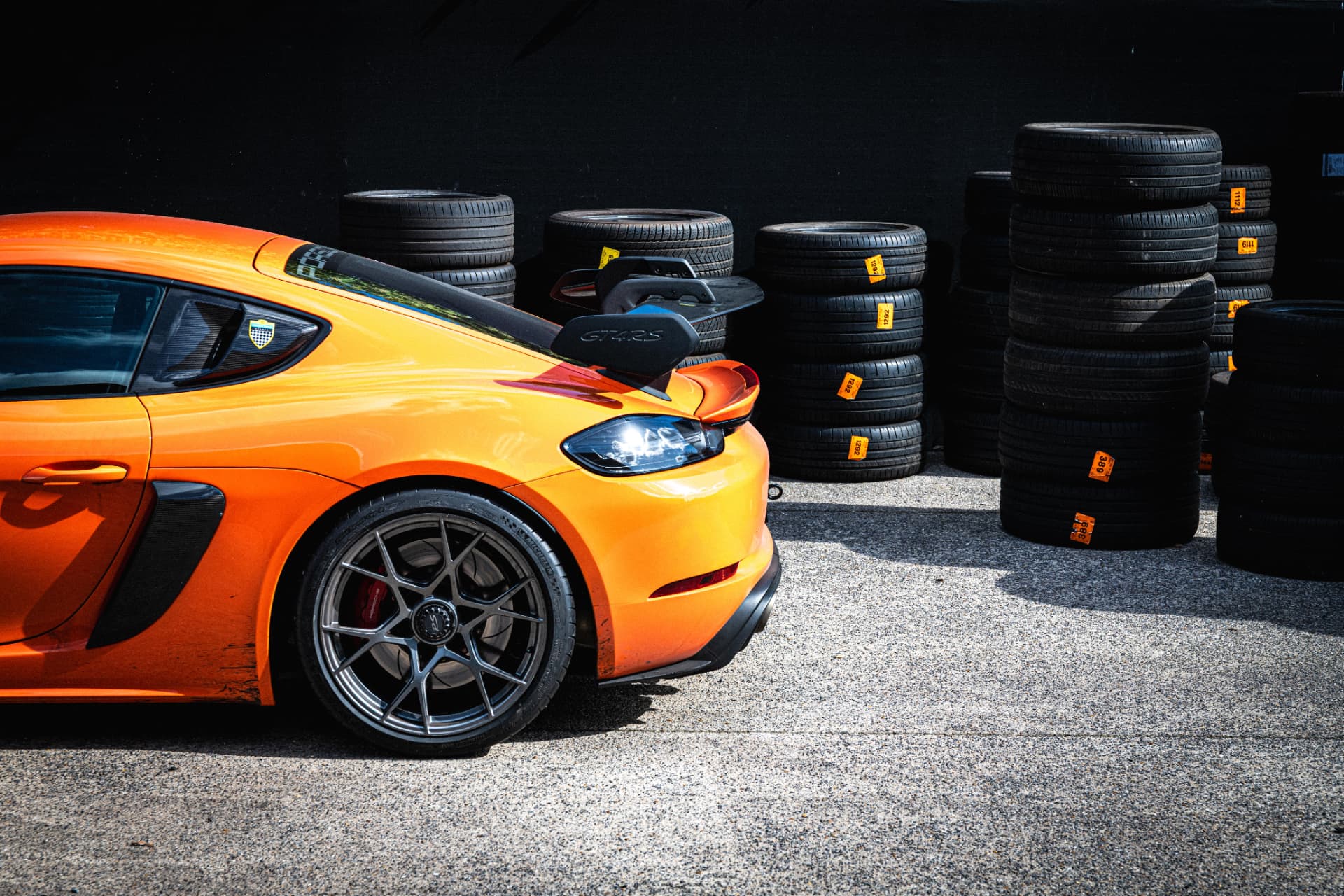 Heinz Performance - premium wheels and rims Orange Porsche GT4 RS with forged center-lock wheels beside stacked racing tires at Heinz Performance